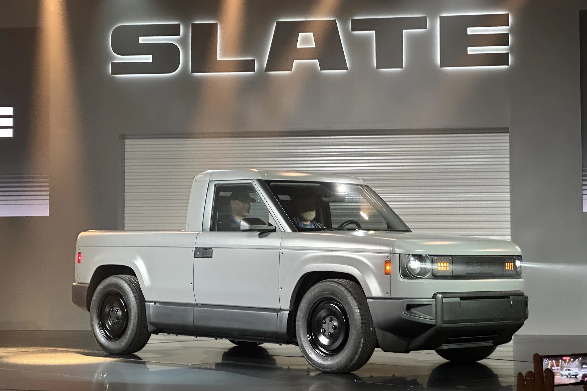 A $25,000 Electric Truck. Built in Indiana. Backed by the World's Second-Richest Man. Slate Auto Just Got Very Real. 2 The Slate Auto electric pickup truck in its bare grey composite finish at the Indiana factory reveal event, representing the opening of preorders at $24,950 on June 24 2026.