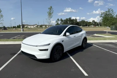 The 2026 Tesla Model Y in white showing the redesigned slim headlights and updated front fascia of the Juniper refresh, parked on a clean surface against a neutral background.