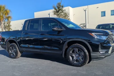 A Honda Ridgeline TrailSport pickup truck parked at a Honda dealership lot, representing the model that will be pulled from production until late 2028 due to emissions standards.