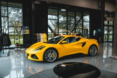 A Lotus Emira sports car parked at the Lotus factory in Hethel, Norfolk, representing the model that will switch to a new hybrid V6 powertrain alongside a revived Esprit V8 supercar.