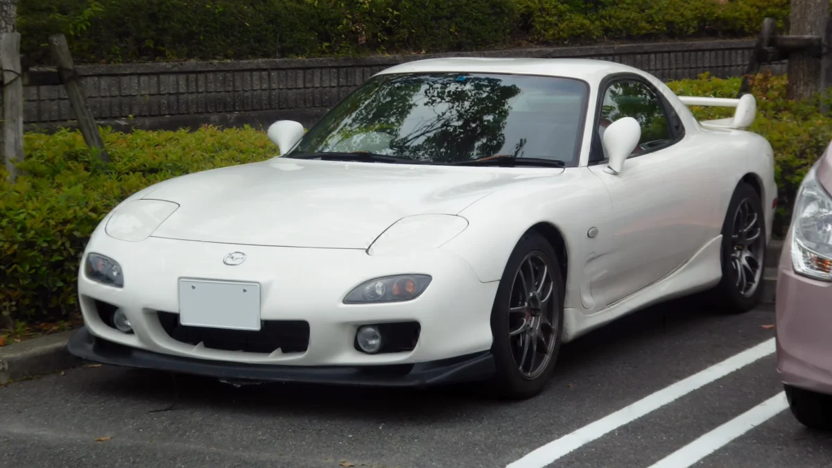 A white third-generation Mazda RX-7 FD with factory body kit and dark alloy wheels, parked in Japan, representing one of the final examples of the rotary-engined sports car that ended production in 2002