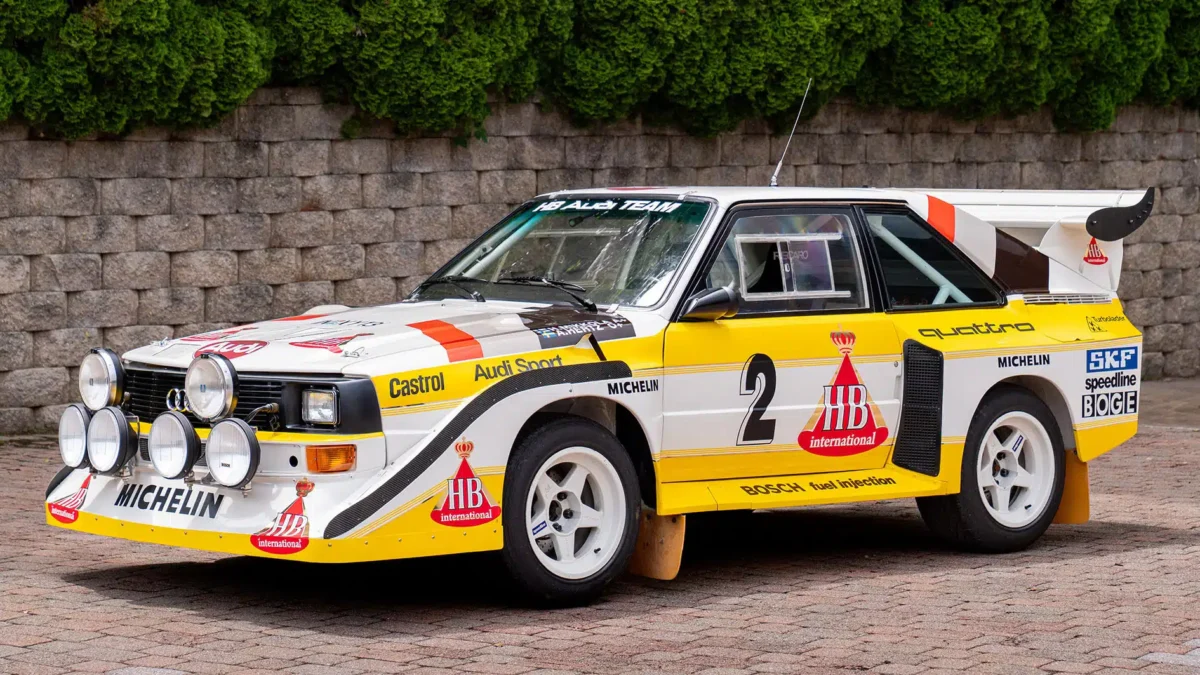 An Audi Quattro S1 at full attack on a WRC stage, its four-wheel drive system throwing gravel as it corners, representing the decision that rewrote the rules of rallying