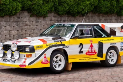 An Audi Quattro S1 at full attack on a WRC stage, its four-wheel drive system throwing gravel as it corners, representing the decision that rewrote the rules of rallying