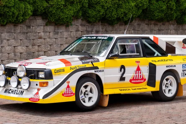 An Audi Quattro S1 at full attack on a WRC stage, its four-wheel drive system throwing gravel as it corners, representing the decision that rewrote the rules of rallying