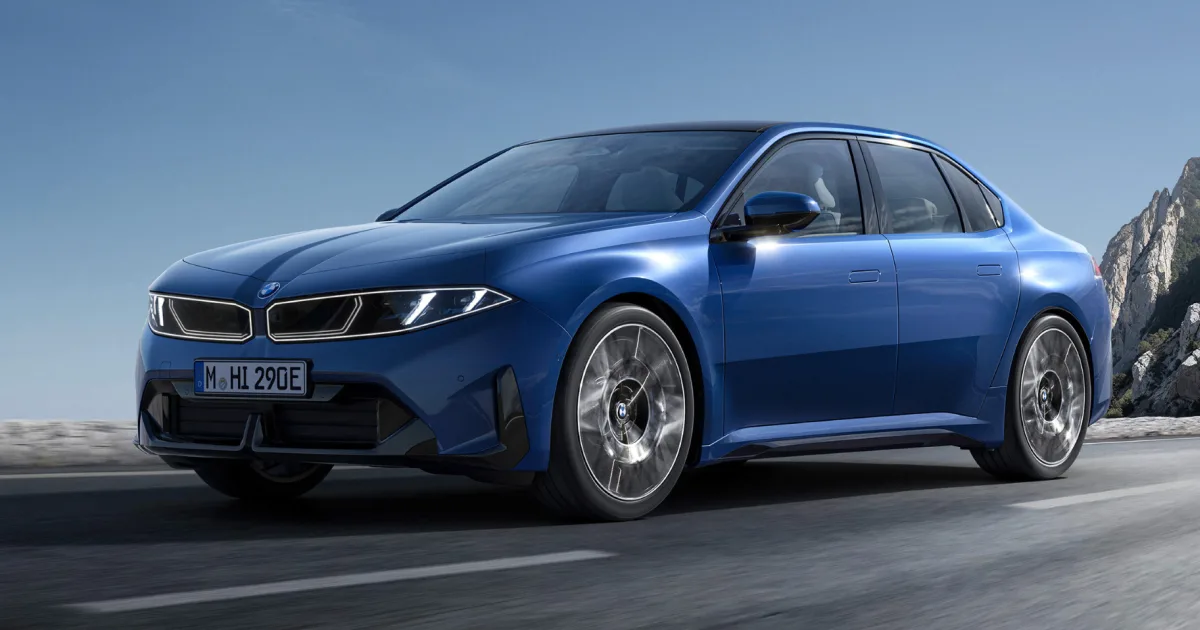A Marina Bay Blue BMW i3 electric sedan photographed in dynamic three-quarter front view on an open road with a rocky mountain backdrop, showcasing the Neue Klasse platform's clean, minimalist exterior design with closed grille and aerodynamic alloy wheels.