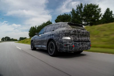 A 2027 BMW X5 G65 luxury SUV in pre-production camouflage being tested at BMW's Plant Spartanburg in South Carolina ahead of its August 2026 production launch with five powertrain options.