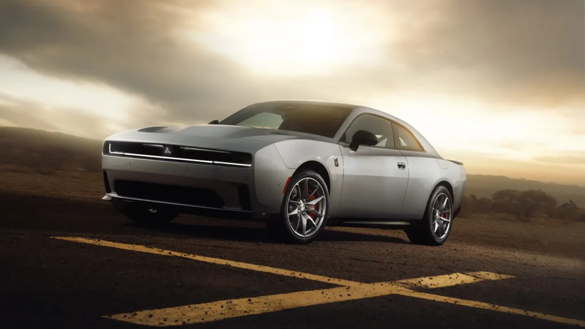 A silver eighth-generation Dodge Charger two-door muscle car photographed at sunset on an open road, with dramatic clouds and a desert landscape behind it.