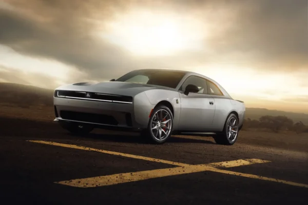 A silver eighth-generation Dodge Charger two-door muscle car photographed at sunset on an open road, with dramatic clouds and a desert landscape behind it.
