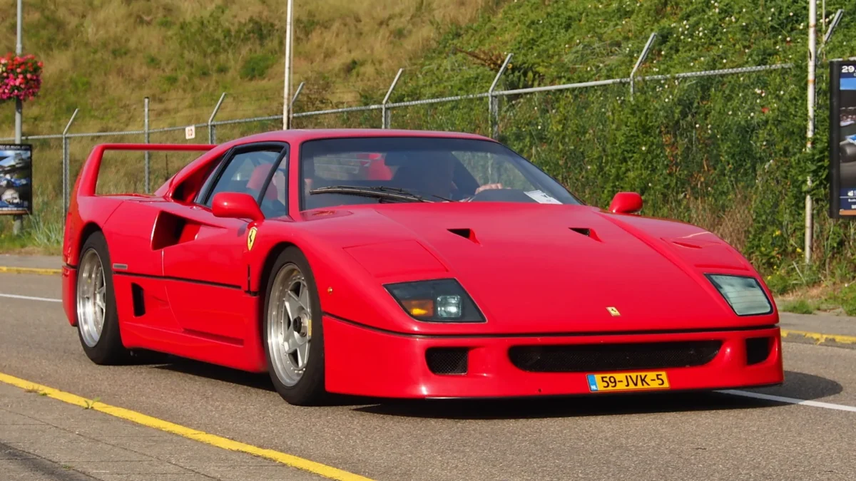 A red Ferrari F40 on a road, representing the last car personally approved by Enzo Ferrari before his death in 1988, photographed in its original uncompromising specification