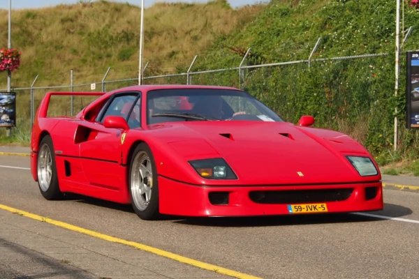 A red Ferrari F40 on a road, representing the last car personally approved by Enzo Ferrari before his death in 1988, photographed in its original uncompromising specification