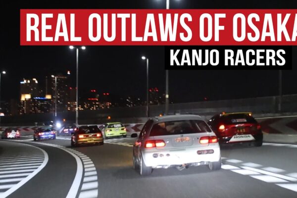 A pack of livery-covered Honda Civics running the Kanjo Loop on the Hanshin Expressway in Osaka at night, captured from behind as the No Good Racing Kanjozoku crew sweeps through a banked corner with the city skyline glowing in the background.
