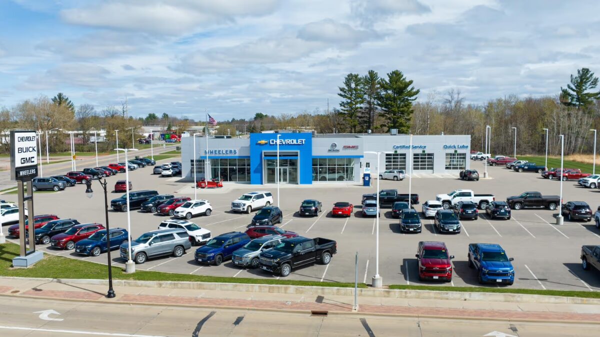 An aerial view of a Chevrolet, Buick and GMC dealership lot filled with rows of Silverado pickup trucks, SUVs and a few sedans parked outside the showroom.