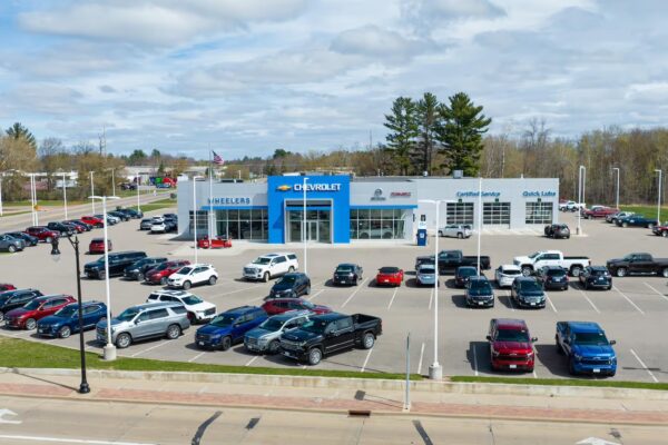 An aerial view of a Chevrolet, Buick and GMC dealership lot filled with rows of Silverado pickup trucks, SUVs and a few sedans parked outside the showroom.