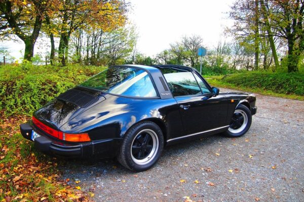 A 1980s Porsche 911 SC on an open road, representing the generation of 911 that CEO Peter Schutz saved from cancellation in 1981 when he overruled Porsche's plan to replace it with the 928