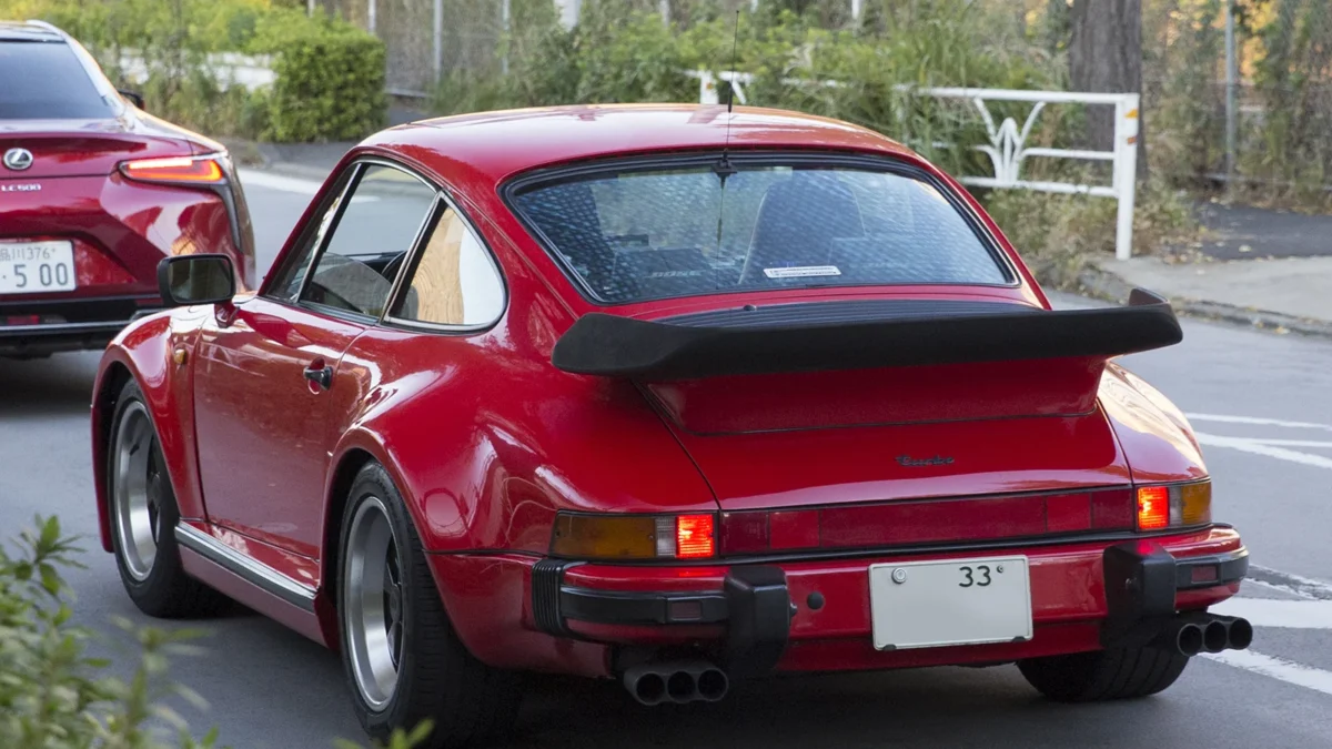 A 1975 Porsche 930 Turbo in Guards Red showing its iconic whale tail spoiler and widened rear arches, the car whose turbocharged engine and rear-heavy layout made it the most feared production car of its era
