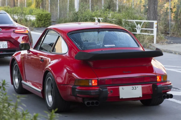A 1975 Porsche 930 Turbo in Guards Red showing its iconic whale tail spoiler and widened rear arches, the car whose turbocharged engine and rear-heavy layout made it the most feared production car of its era