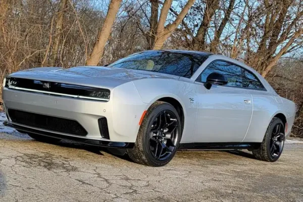 A silver 2026 Dodge Charger SIXPACK two-door muscle car with black alloy wheels parked on a paved surface with bare winter trees in the background.