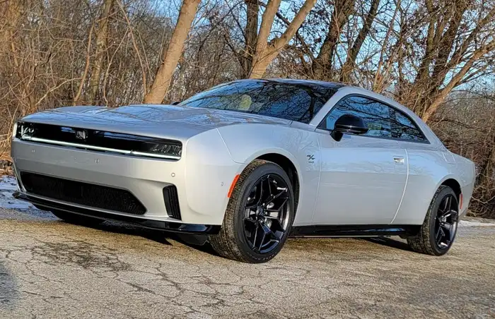 A silver 2026 Dodge Charger SIXPACK two-door muscle car with black alloy wheels parked on a paved surface with bare winter trees in the background.