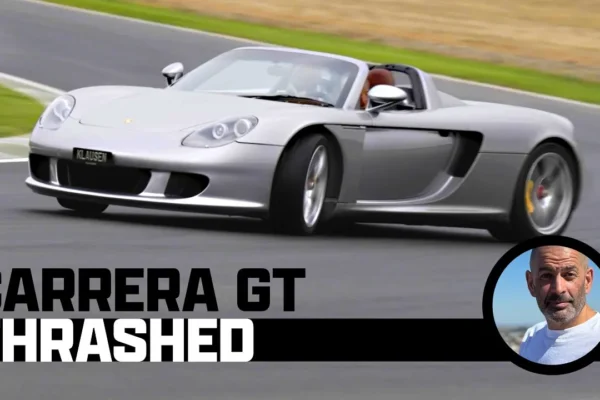 A Porsche Carrera GT on track at the Ascari Circuit in Spain on a damp surface showing the rear spoiler raised and the V10 supercar in motion.